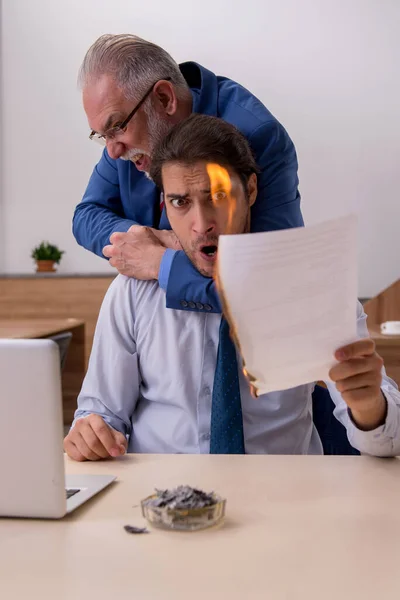 Junger männlicher Mitarbeiter und alter Chef verbrennen Papiere am Arbeitsplatz — Stockfoto