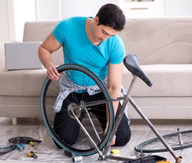 Evde bisiklet tamir eden genç bir adam.