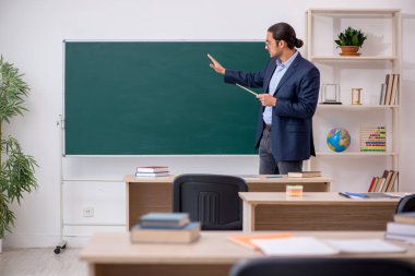 Genç erkek öğretmen yeşil panonun önünde.