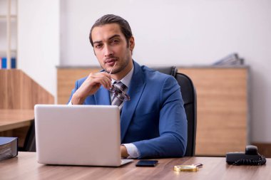 Genç erkek çalışan işyerinde oturuyor.