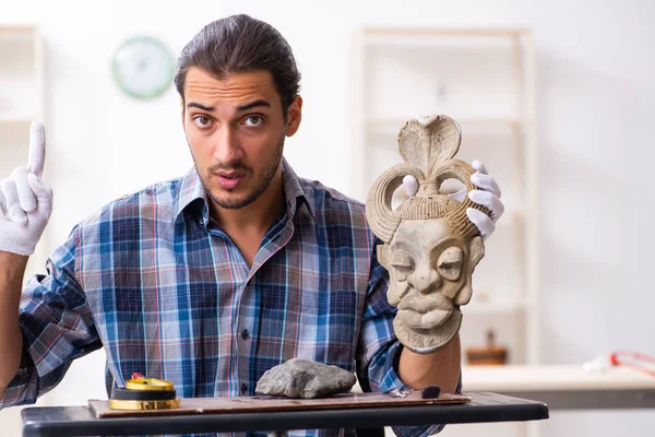 Joven arqueólogo masculino estudiando la antigua máscara de piedra africana —  Fotos de Stock