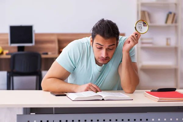 Giovane studente maschio preparazione per gli esami a casa tenendo loupe — Foto Stock