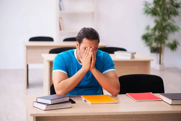 Utmattad manlig student förbereder sig för tentorna i klassrummet — Stockfoto