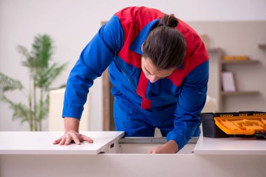 Genç erkek müteahhit içeride masa onarıyor.