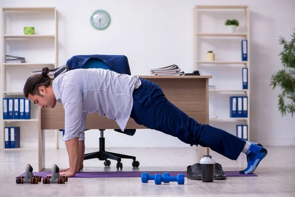 Ung stilig manlig anställd gör övningar på kontoret — Stockfoto