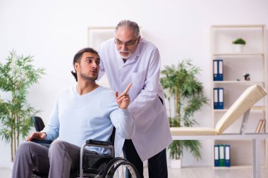 Tekerlekli sandalyedeki genç adam ve yaşlı doktor travmatolog.