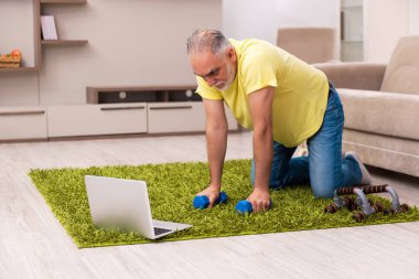 Yaşlı adam evde spor egzersizleri yapıyor.