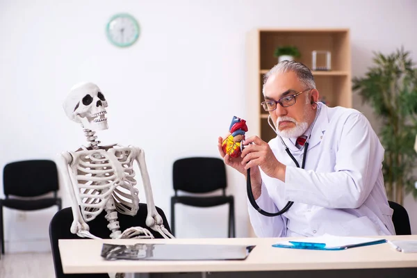 Oude mannelijke arts cardioloog en skelet patiënt in de kliniek — Stockfoto