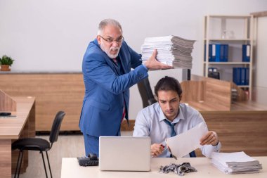 Genç erkek çalışan ve yaşlı patron iş yerinde kağıtları yakıyor.