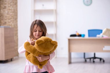 Küçük kız elinde oyuncak ayı klinikte doktoru bekliyor.
