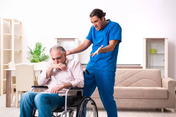 Oude man in rolstoel en jonge slechte verzorger binnen — Stockfoto