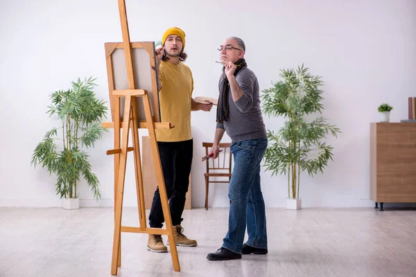 Old man taking lesson from young painter