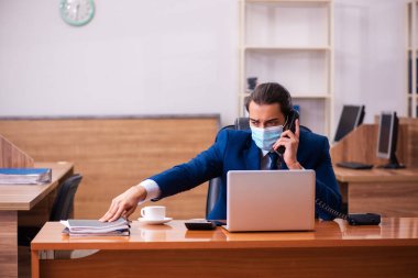 Ofiste maske takan genç bir erkek çalışan.