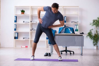Genç yakışıklı çalışan ofiste spor egzersizleri yapıyor.