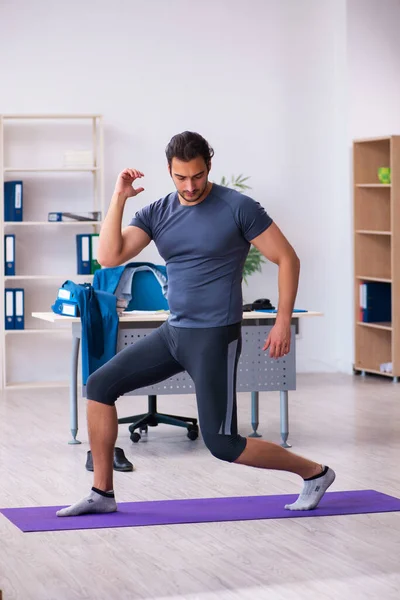 Young handsome employee doing sport exercises in the office