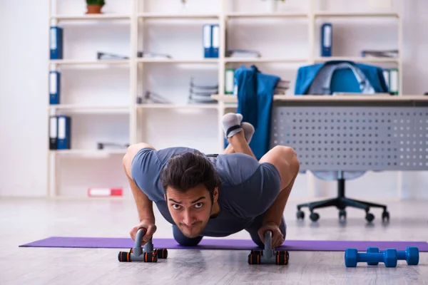 Joven empleado guapo haciendo ejercicios deportivos en la oficina — Foto de Stock