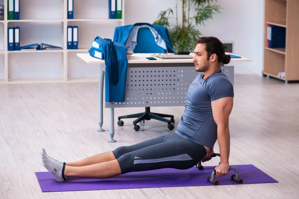 Young handsome employee doing sport exercises in the office