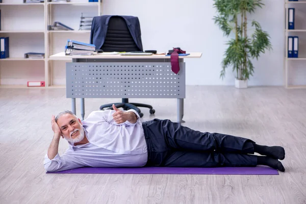 Verouderde mannelijke werknemer doet fysieke oefeningen tijdens de pauze — Stockfoto