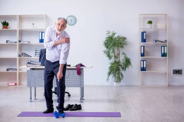 Verouderde mannelijke werknemer doet fysieke oefeningen tijdens de pauze — Stockfoto