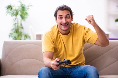 Genç adam evde joystick oynuyor.