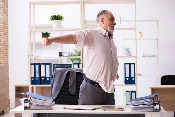 Vecchio dipendente maschio che fa esercizi fisici sul posto di lavoro — Foto Stock