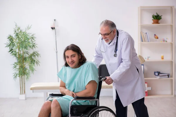 Jonge mannelijke patiënt in rolstoel en ervaren arts-traumatoloog — Stockfoto