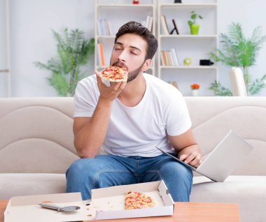 Pizza yiyen adam evde yemek yiyor, dinleniyor.