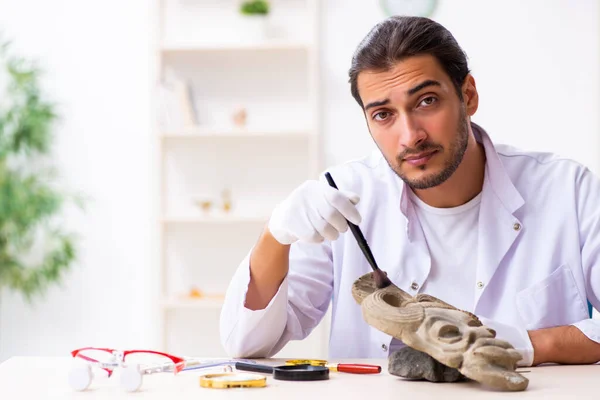 Joven arqueólogo masculino estudiando la antigua máscara de piedra africana — Foto de Stock