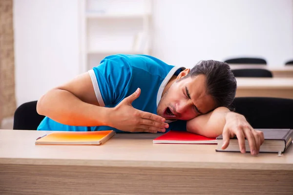 Estudante masculino exausto se preparando para os exames em sala de aula — Fotografia de Stock