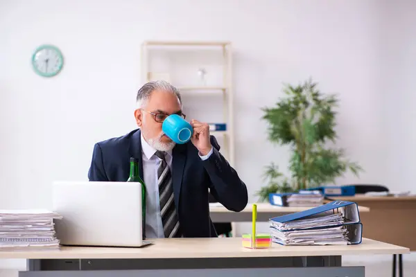 Oude mannelijke werknemer drinkt alcohol op kantoor — Stockfoto