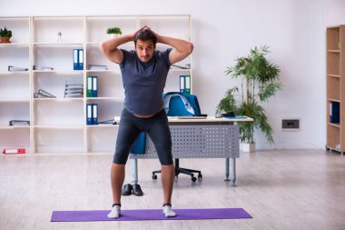 Genç yakışıklı çalışan ofiste spor egzersizleri yapıyor.