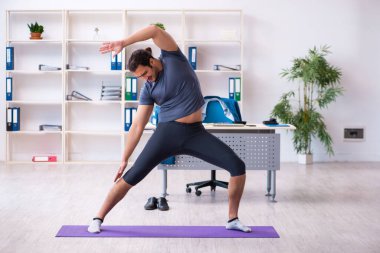 Genç yakışıklı çalışan ofiste spor egzersizleri yapıyor.