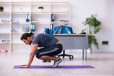 Genç yakışıklı çalışan ofiste spor egzersizleri yapıyor.
