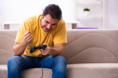 Genç adam evde joystick oynuyor.