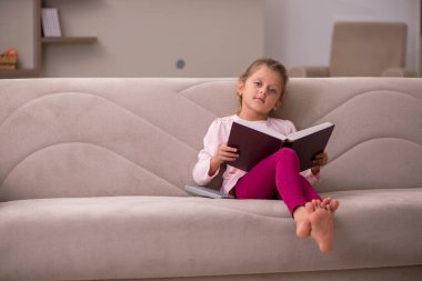 Evde kitap okuyan küçük bir kız.