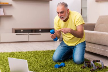 Yaşlı adam evde spor egzersizleri yapıyor.