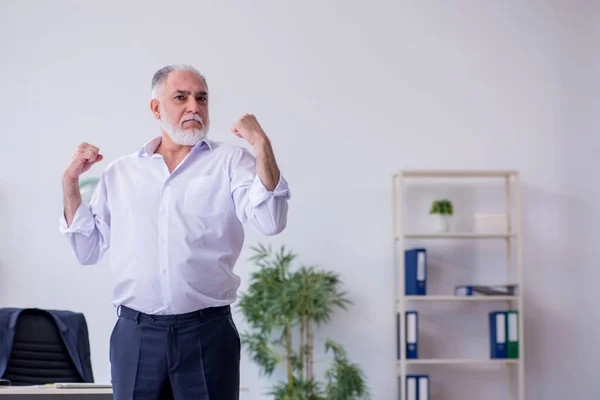 Verouderde mannelijke werknemer doet fysieke oefeningen tijdens de pauze — Stockfoto