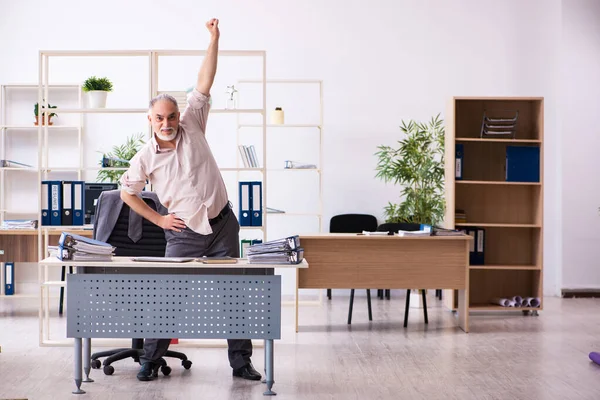 Starý muž zaměstnanec dělá fyzická cvičení na pracovišti — Stock fotografie