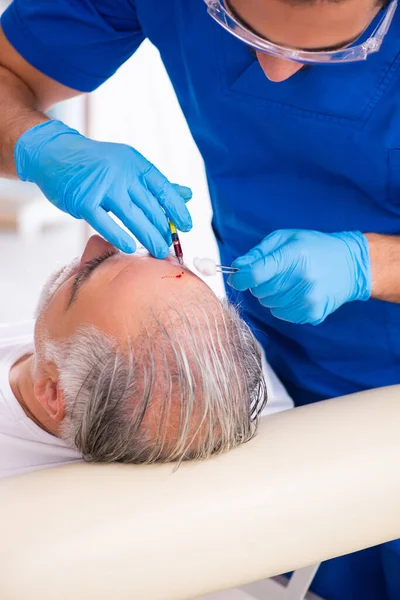 Old man visiting young male doctor in hair transplantation conce — Stock Photo, Image