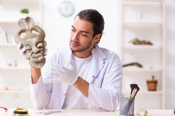 Jonge mannelijke archeoloog bestudeert het oude Afrikaanse steenmasker — Stockfoto