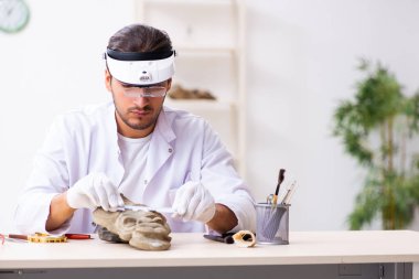 Genç erkek arkeolog eski Afrika taş maskesi üzerinde çalışıyor.