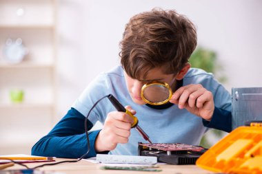 Çocuk atölyede bilgisayar tamir ediyor.