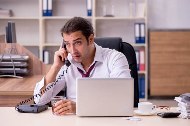 Genç erkek çalışan ofiste alkol içiyor.