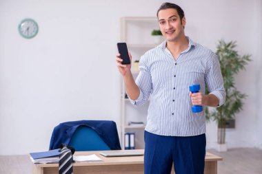 Genç yakışıklı erkek çalışanımız ofiste egzersiz yapıyor.