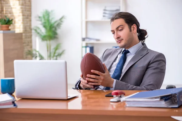 Молодой сотрудник с мячом для регби в офисе — стоковое фото
