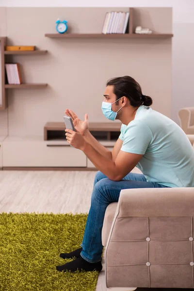 Молодой человек смотрит телевизор дома во время пандемии — стоковое фото