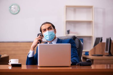 Ofiste maske takan genç bir erkek çalışan.