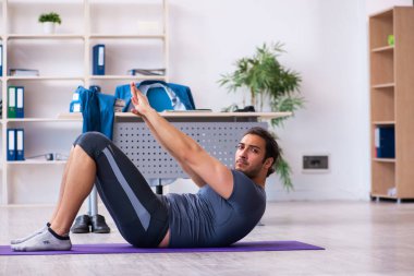 Genç yakışıklı çalışan ofiste spor egzersizleri yapıyor.