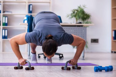 Genç yakışıklı çalışan ofiste spor egzersizleri yapıyor.