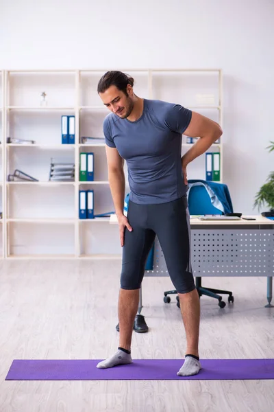 Young handsome employee doing sport exercises in the office — Stock Photo, Image